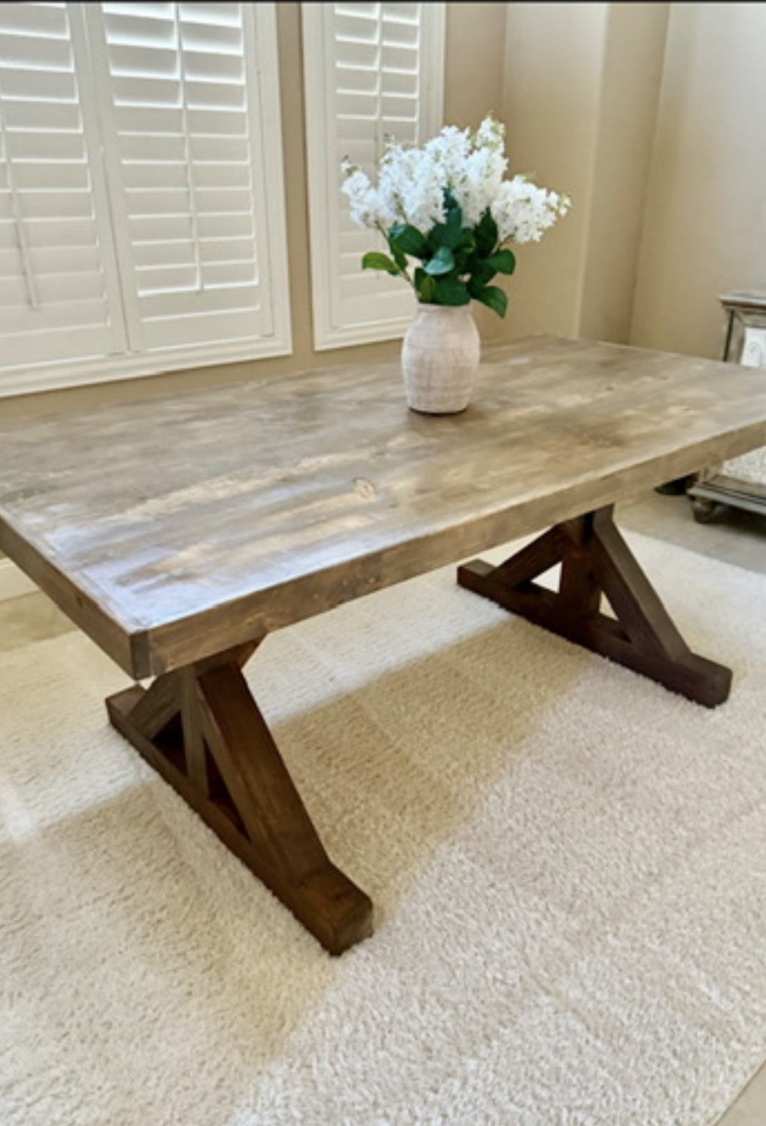 Weathered gray farmhouse table with a dark trestle base in a bright dining room